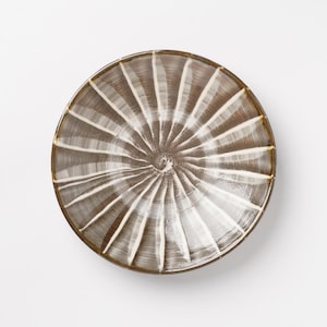 May include: A round ceramic bowl featuring a dark brown glaze with a series of radiating white brushstroke lines that extend from the center toward the outer rim, creating a sunburst pattern across the interior surface of the dish.