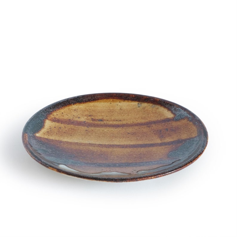 May include: A brown and blue ceramic plate with a striped design. The plate is round and has a slightly raised rim.