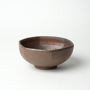 May include: A brown ceramic bowl with a speckled glaze. The bowl has a slightly rounded shape and a wide, flat base.
