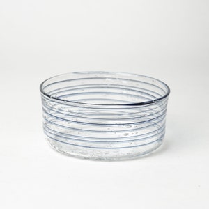May include: A clear glass bowl with blue stripes and air bubbles. The bowl is round and has a smooth, polished finish.