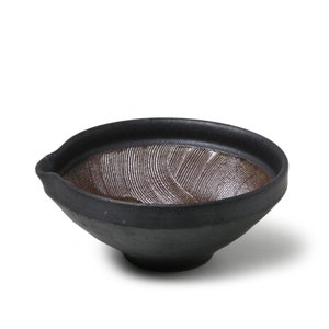 May include: A black ceramic suribachi, a Japanese mortar and pestle, with a textured, ridged interior. The suribachi is designed for grinding and crushing ingredients.