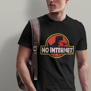 Könnte beinhalten: Schwarzes T-Shirt mit einem pixeligen Dinosaurier-Grafik in einem roten Kreis mit dem weißen Schriftzug "NO INTERNET". Das Design erinnert an ein klassisches Filmlogo. Das T-Shirt wird von einer Person getragen.