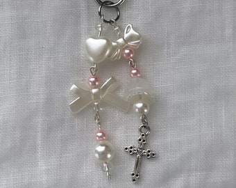 May include: A white and silver charm keychain with a heart, bow, cross, and pearl beads.