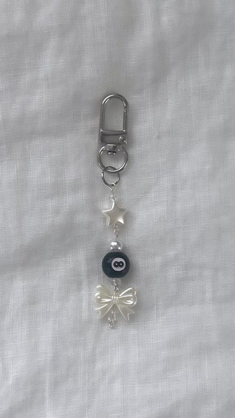 May include: A silver keychain with a black 8-ball charm, a white star charm, and a white bow charm.