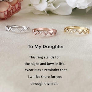 May include: Three rings in silver, rose gold, and gold, each with a zigzag design and small gemstones. The text "To My Daughter" and a message about support are also visible.