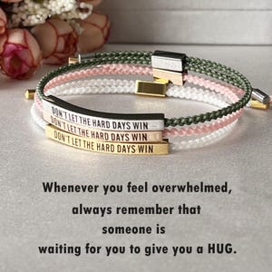 May include: Three bracelets with the text "DON'T LET THE HARD DAYS WIN" in white, silver, and gold. The bracelets have braided bands in green, pink, and white. The image also includes the text: "Whenever you feel overwhelmed, always remember that someone is waiting for you to give you a HUG."