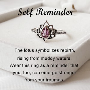 May include: A silver ring with a lotus flower design and a pink gemstone center. The ring has a delicate band with small, clear stones. The text "Self Reminder" is above the ring, with inspirational text below.