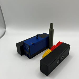 Peut inclure: Un mod&egrave;le bleu et noir d'un g&eacute;n&eacute;rateur avec un mod&egrave;le vert d'un r&eacute;servoir d'essence, le tout pos&eacute; sur un mod&egrave;le noir et rouge d'un rangement.