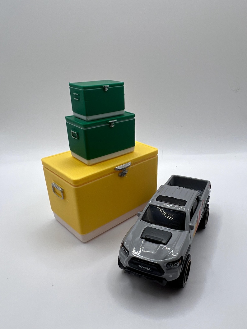 K&ouml;nnte beinhalten: Ein Set aus gelben, gr&uuml;nen und wei&szlig;en K&uuml;hlboxen mit einem grauen Toyota Tacoma Spielzeug-Truck. Die K&uuml;hlboxen sind gestapelt, mit einer gro&szlig;en gelben K&uuml;hlbox unten und zwei gr&uuml;nen K&uuml;hlboxen dar&uuml;ber.