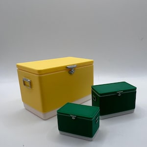 K&ouml;nnte beinhalten: Drei rechteckige K&uuml;hlboxen in verschiedenen Gr&ouml;&szlig;en. Die gr&ouml;&szlig;te ist gelb mit wei&szlig;em Sockel, die mittleren und kleinen K&uuml;hlboxen sind gr&uuml;n mit wei&szlig;en Sockeln. Alle haben silberne Verschl&uuml;sse und Griffe.