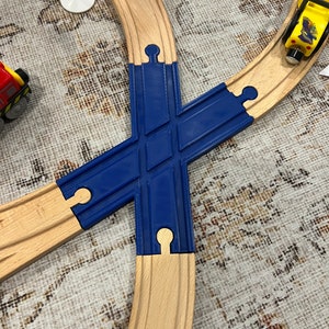 May include: A blue wooden train track intersection with two curved wooden tracks leading into the intersection. The intersection has two openings for the train to go through.