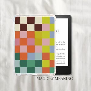 Könnte beinhalten: Eine transparente Schutzhülle für einen E-Reader mit einem farbenfrohen Schachbrettmuster in Braun-, Rosa-, Orange-, Grün- und Gelbtönen. Der E-Reader ist schwarz, und der Bildschirm zeigt Text an. Die Worte "MAGIC & MEANING" stehen unten.