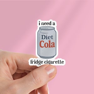 May include: A sticker featuring a Diet Cola can design with the text "i need a" above and "fridge cigarette" below. The can is gray with red and white text, held by a hand against a pink background.