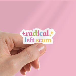 May include: A white sticker with the words "radical left scum" in colorful text. The sticker is held against a pink background. The word "radical" is in pink, blue, and green, while "scum" is in yellow.
