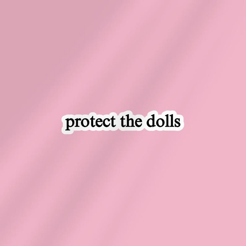 May include: A sticker with the text "protect the dolls" in a black font with a white border. The sticker is set against a soft pink background.