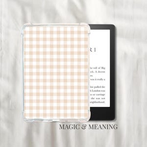 Peut inclure: Une coque de protection transparente avec un motif vichy beige et blanc est sur le côté gauche d'un lecteur ebook noir. Le lecteur affiche du texte. Les mots "MAGIC & MEANING" sont en bas.
