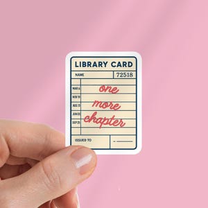 Puede incluir: Una pegatina rectangular que se asemeja a una tarjeta de biblioteca, sobre un fondo rosa. La pegatina presenta las palabras "LIBRARY CARD" en la parte superior, con el texto "one more chapter" en cursiva. También son visibles fechas y un número.