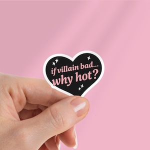 Puede incluir: Una pegatina en forma de corazón con el texto "if villain bad... why hot?" en blanco y rosa sobre un fondo negro. La pegatina se sostiene sobre un fondo rosa.