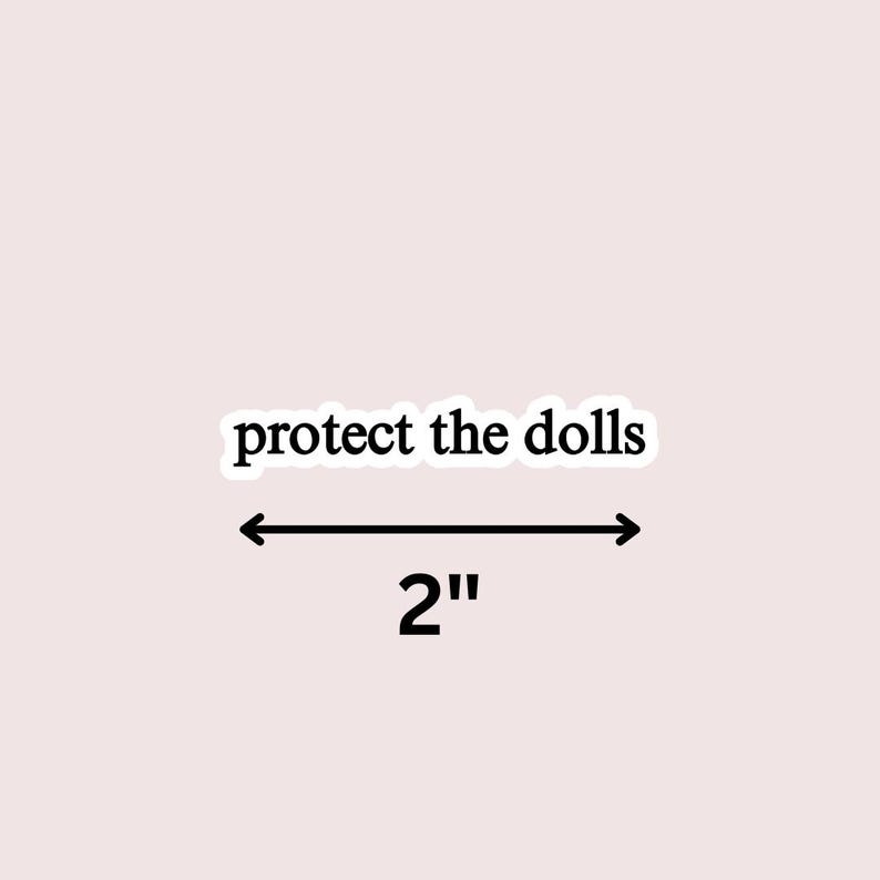May include: A sticker with the text "protect the dolls" in a black, bold font. The sticker is 2 inches (5 cm) wide, indicated by a black arrow and the number 2. The background is a light pink color.