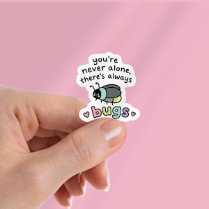 May include: A die-cut sticker featuring a cartoon beetle with a black, blue, and yellow body. The text reads, you're never alone, there's always bugs, with the word bugs in multicoloured letters and two small pink hearts on either side.