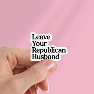 May include: White sticker with the text "Leave Your Republican Husband" in a bold, sans-serif font. The sticker is held between fingers against a pink background.