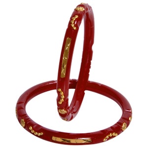 May include: Two red bangles with gold-colored accents. The bangles have a glossy finish and are decorated with small, round gold embellishments and rectangular gold plates. The design is symmetrical and the bangles are displayed against a white background.