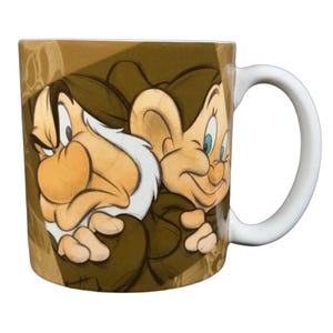 Può includere: Tazza in ceramica bianca con un'illustrazione a cartoni animati di due nani di Biancaneve. I nani sono raffigurati in tonalità di marrone, beige e bianco, uno con un'espressione scontrosa e l'altro sorridente. La tazza ha un manico bianco.