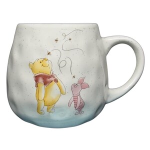 Puede incluir: Taza de cerámica blanca con una ilustración de Winnie the Pooh y Piglet mirando abejas. La taza tiene un asa grande y un acabado moteado, con un degradado azul claro en la parte inferior.