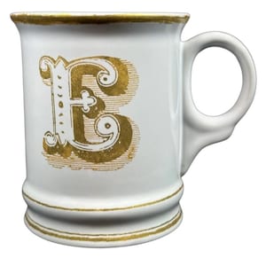 May include: White ceramic mug featuring a gold letter "B" and gold trim. The mug has a rounded handle and a flared base. The gold letter is ornate and stylized. A classic and decorative item. The mug is suitable for hot or cold beverages.