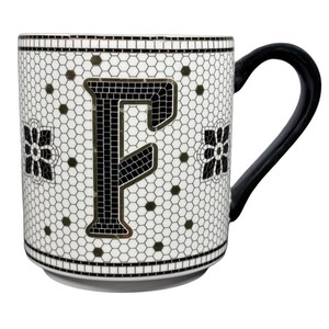 Può includere: Tazza in ceramica bianca con manico nero e design a mosaico. La tazza presenta una grande lettera "F" nera al centro, circondata da un motivo di piccoli esagoni neri e accenti floreali. La tazza ha un bordo e una base neri.