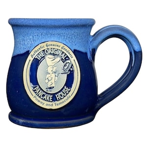 May include: A ceramic mug with a blue and navy glaze. The mug features a circular emblem with the text "The Original Pancake House" and an illustration of a chef flipping pancakes. The mug has a large handle.