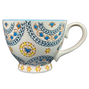 May include: White ceramic teacup with a blue interior and a large handle. The cup is decorated with blue and yellow floral patterns and a blue rim. The design includes a series of blue paisley shapes and yellow flowers.