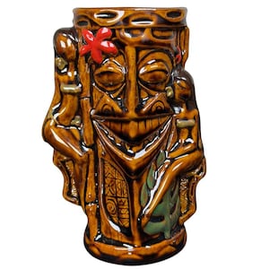 May include: Brown ceramic tiki mug with a smiling face, bamboo accents, and two figures on the sides. The mug features a red flower and green leaf details. This unique mug is perfect for tropical drinks.