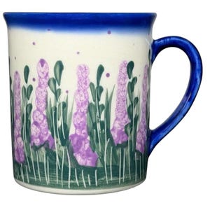 Puede incluir: Una taza de cerámica blanca con un asa negra y el texto "But First, Coffee" en negrita negra. La taza está llena de un líquido oscuro, probablemente café, y se encuentra sobre una superficie clara.