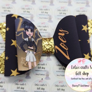 May include: A handmade hair bow featuring a cartoon character, gold glitter, and star accents. The bow is navy blue with gold stars and the name "Zoey" in gold script. The bow is from Lola's Crafts & Gift Shop.