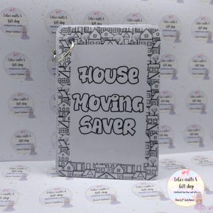 May include: A clear acrylic keyring with the text "HOUSE MOVING SAVER" in black. The design features a border of black and white houses. A silver-coloured keyring is attached. The item is rectangular in shape.