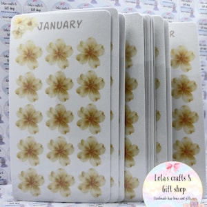 May include: A collection of white cards, each adorned with light brown floral patterns and the word "JANUARY" on the top card. The cards are from Lola's Crafts & Gift Shop, offering handmade hair bows and gifts. The cards are stacked together.
