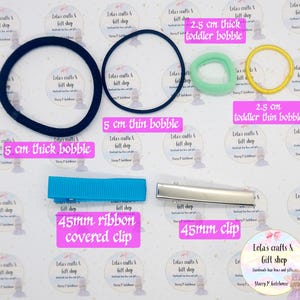 May include: Assortment of hair accessories including black and navy blue bobbles, a light blue ribbon-covered clip, a silver clip, and green and yellow toddler bobbles. The image also includes text that reads "Lola's crafts & gift shop".
