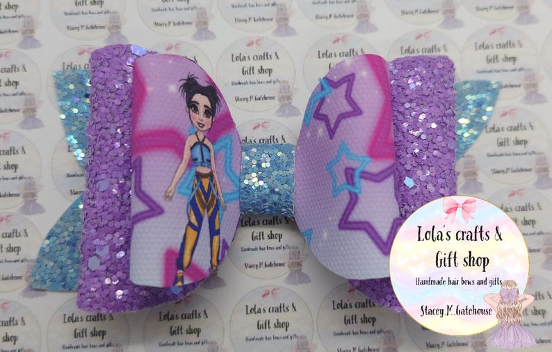 May include: A handmade hair bow featuring a cartoon character design. The bow has a purple glitter base with a light blue glitter accent. The center features a cartoon character with star accents. The bow is from Lola's Crafts & Gift Shop.