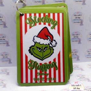 May include: A stack of green-edged cards with a red and white striped background. The cards feature the Grinch wearing a Santa hat and the words "Stocking Stuffing Challenge". A metal ring holds the cards together.
