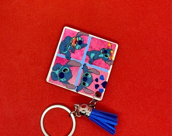Puede incluir: Un llavero azul y rosa con un personaje de dibujos animados en múltiples poses. El llavero tiene un borla azul y un anillo plateado.