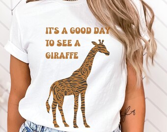 Może przedstawiać: Biała koszulka z ilustracją brązowej i pomarańczowej żyrafy i tekstem "It's a good day to see a giraffe".