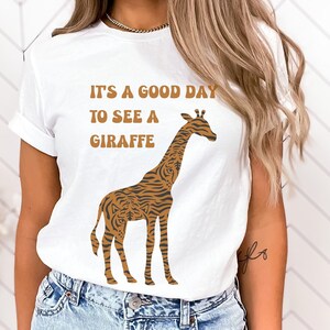 May include: White t-shirt with a brown and orange giraffe illustration and the text "It's a good day to see a giraffe".