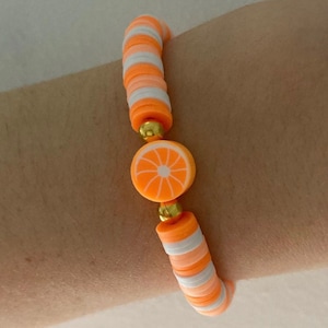 May include: Orange slice charm bracelet with white and orange beads. The bracelet is made of polymer clay and has a gold accent.
