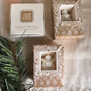 Puede incluir: Tres cajas con figuras de ángeles. Una caja es blanca con un diseño dorado y el texto "Margaret Furlong, Oh, Sweetest Heart". Las otras dos cajas tienen un patrón dorado y blanco y contienen una figura de ángel blanca.