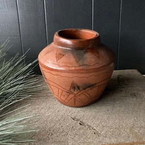 May include: A terracotta pot with a geometric design. The pot is brown with a dark brown glaze and has a wide mouth.