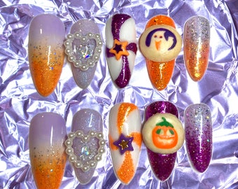 May include: Set of ten Halloween-themed fake nails with various designs. The nails are decorated with orange, purple, white, and glitter. Some nails feature 3D embellishments, including a heart, a star, a ghost, a pumpkin, and a candy cane.