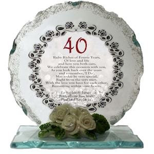 Może przedstawiać: Przezroczysta szklana tablica na 40. rocznicę, z dekoracyjną krawędzią i kwiatowymi detalami. Numer "40" jest czerwony, a tekst celebruje czterdzieści lat miłości. Bukiet białych róż znajduje się u podstawy.