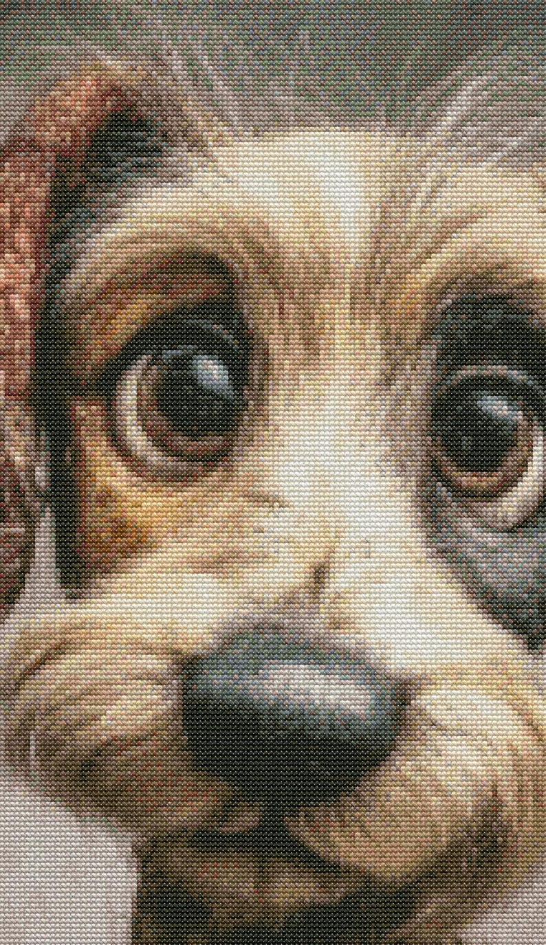 May include: Close-up of a cross-stitch portrait of a dog's face. The dog has large, expressive brown eyes, a black nose, and a mix of tan, brown, and white fur. The stitching creates a detailed, textured effect.