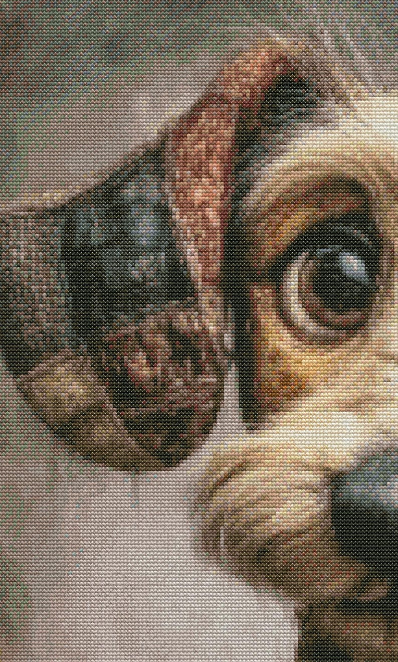 May include: Close-up of a dog's face, showcasing detailed cross-stitch embroidery. The dog's eye is a deep brown, with tan and brown fur. The ear is a mix of brown and black, with a textured appearance. The background is a light beige.